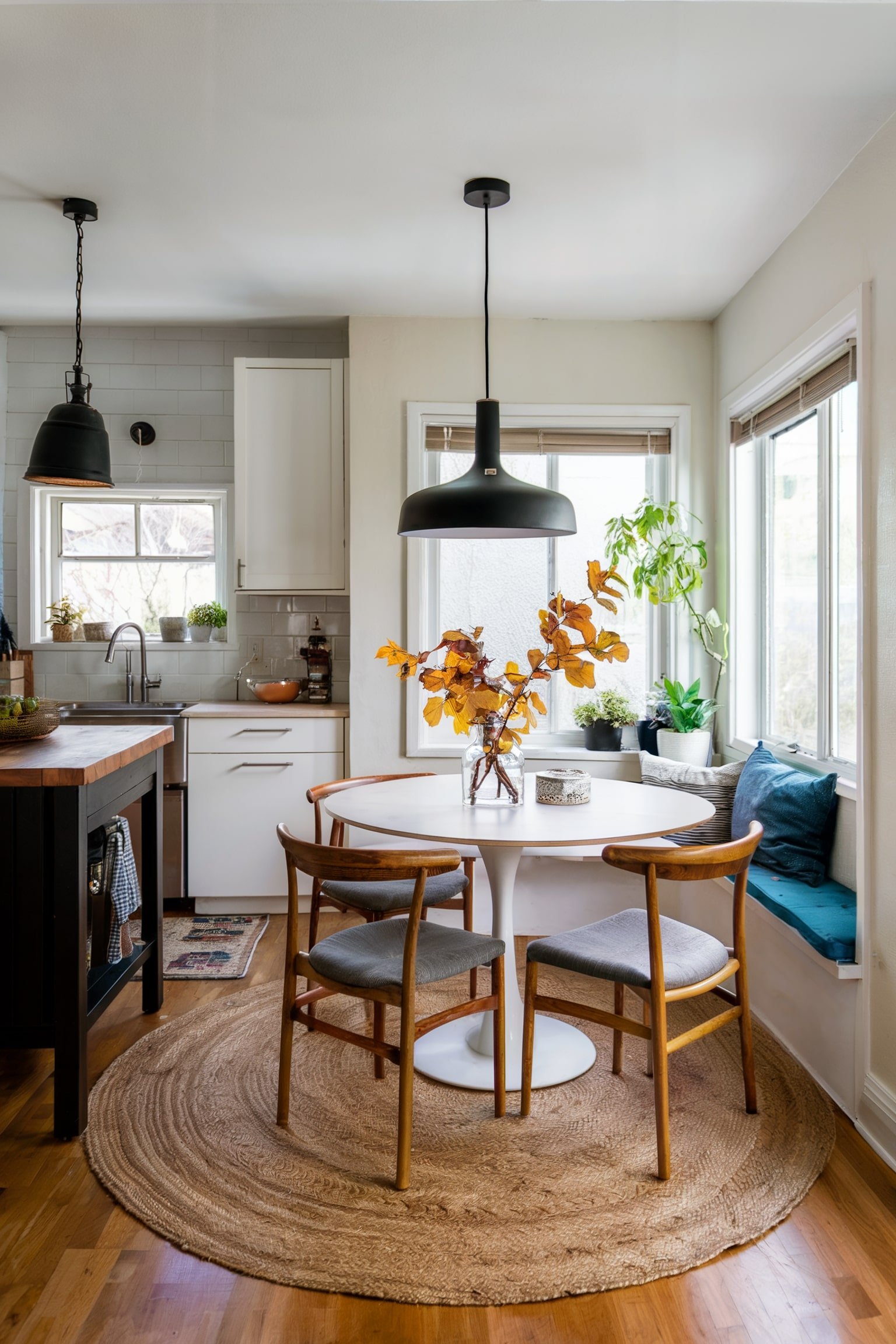 Round white table with wooden chairs, pendant light, and window seat with plants