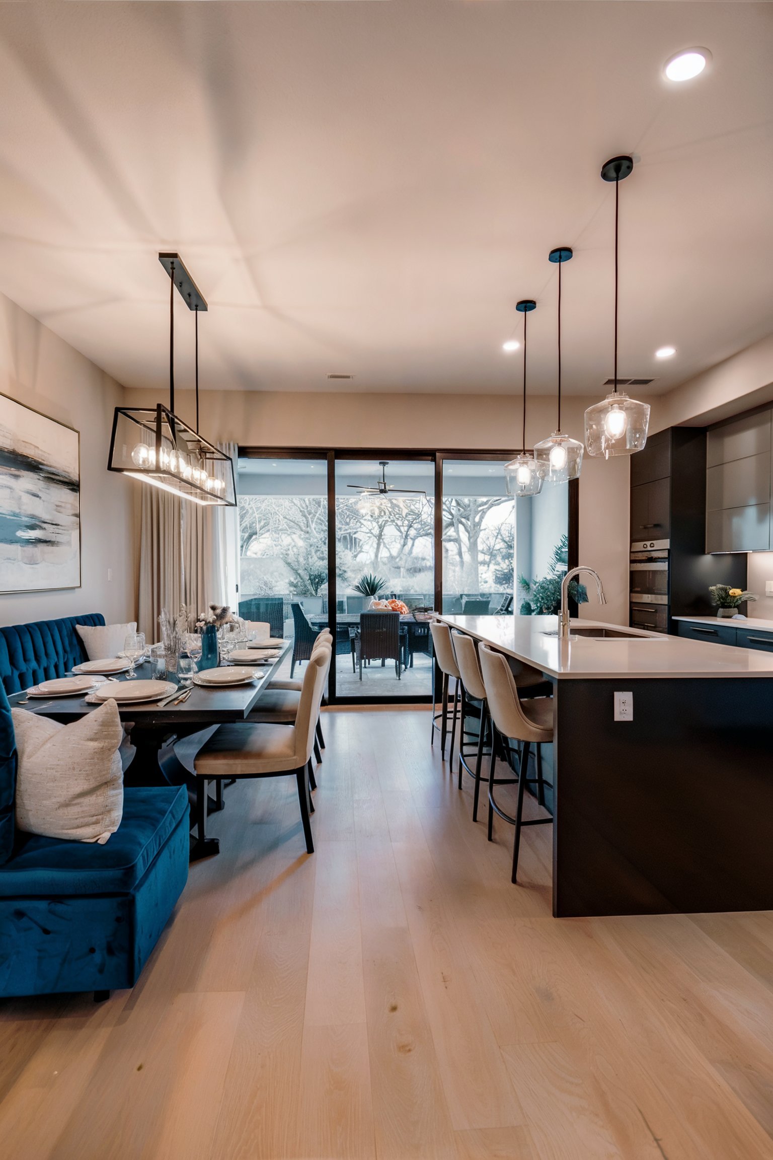 Modern dining space with blue banquette, large glass doors, and sleek lighting over table setting