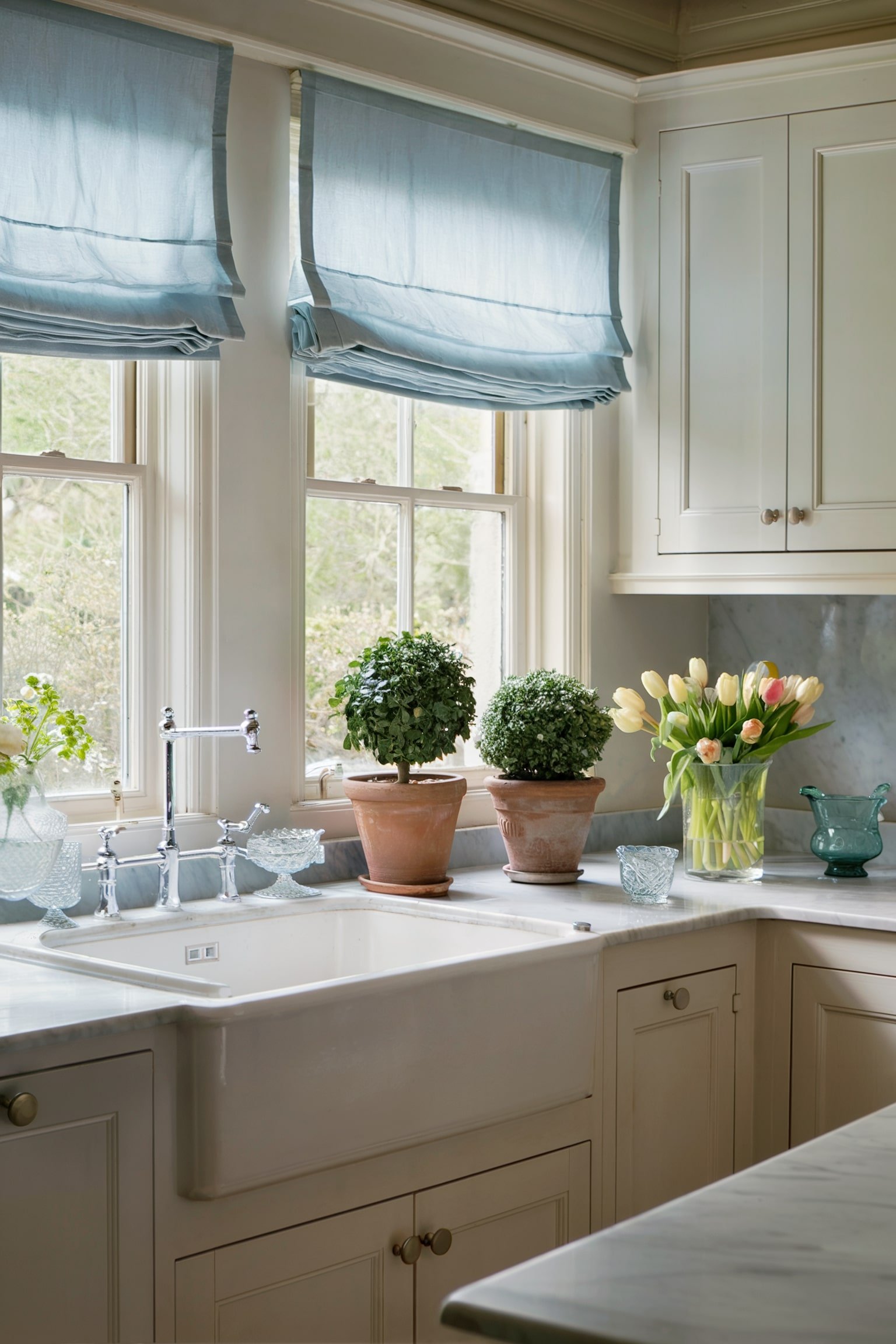 Kitchen sink with light blue Roman shades and potted plants on the windowsill