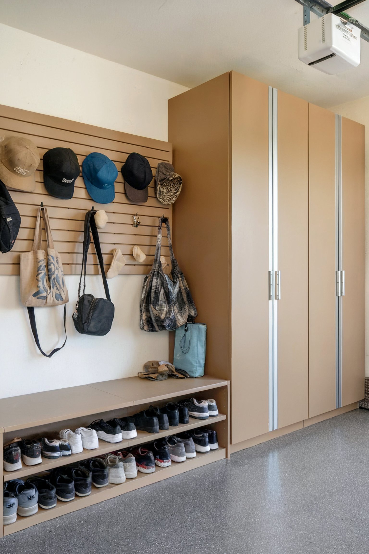 Brown cabinets with a shoe shelf and hooks for bags and hats in a garage mudroom