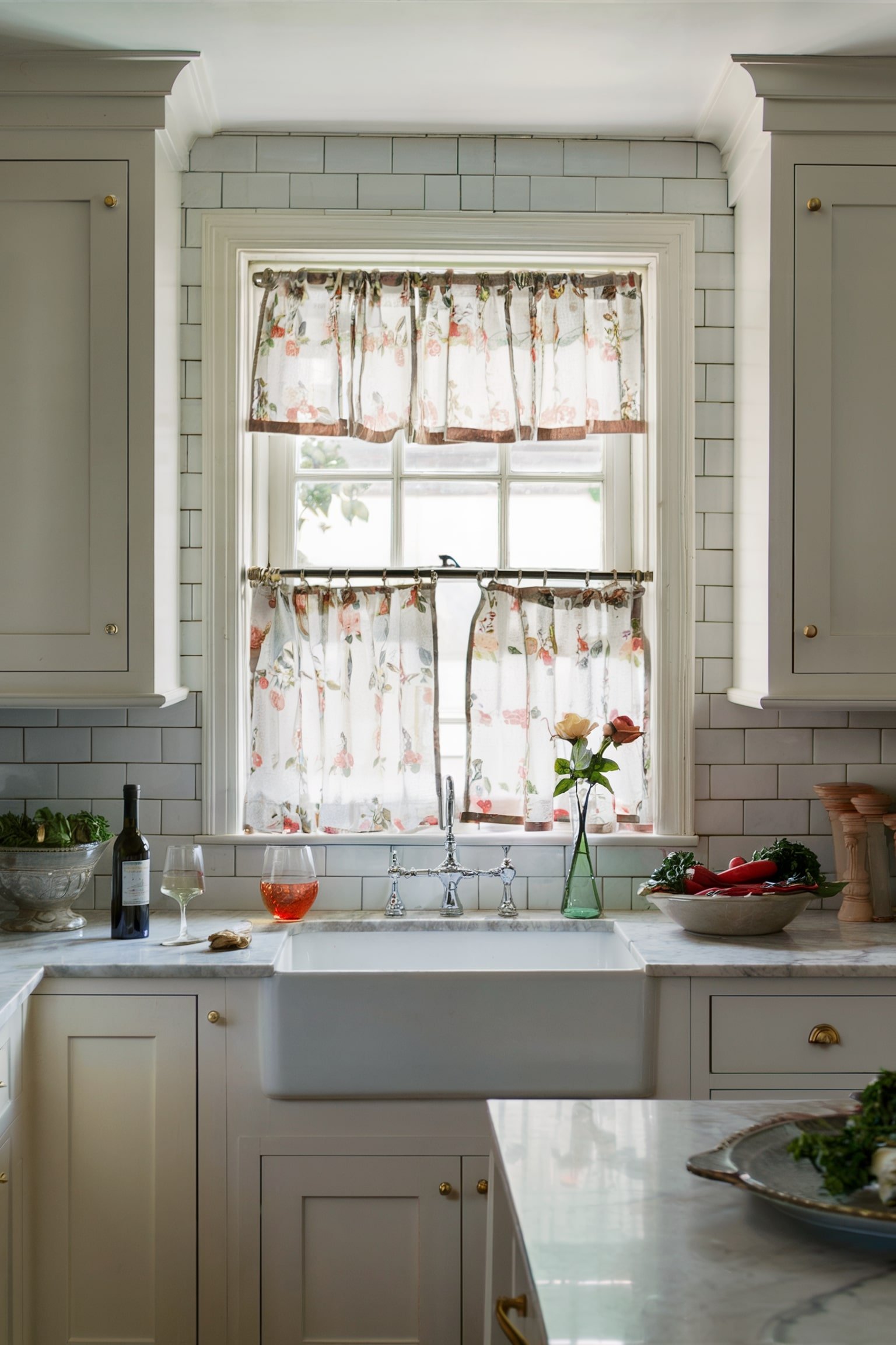 Kitchen window with floral cafรฉ curtains and a farmhouse sink below