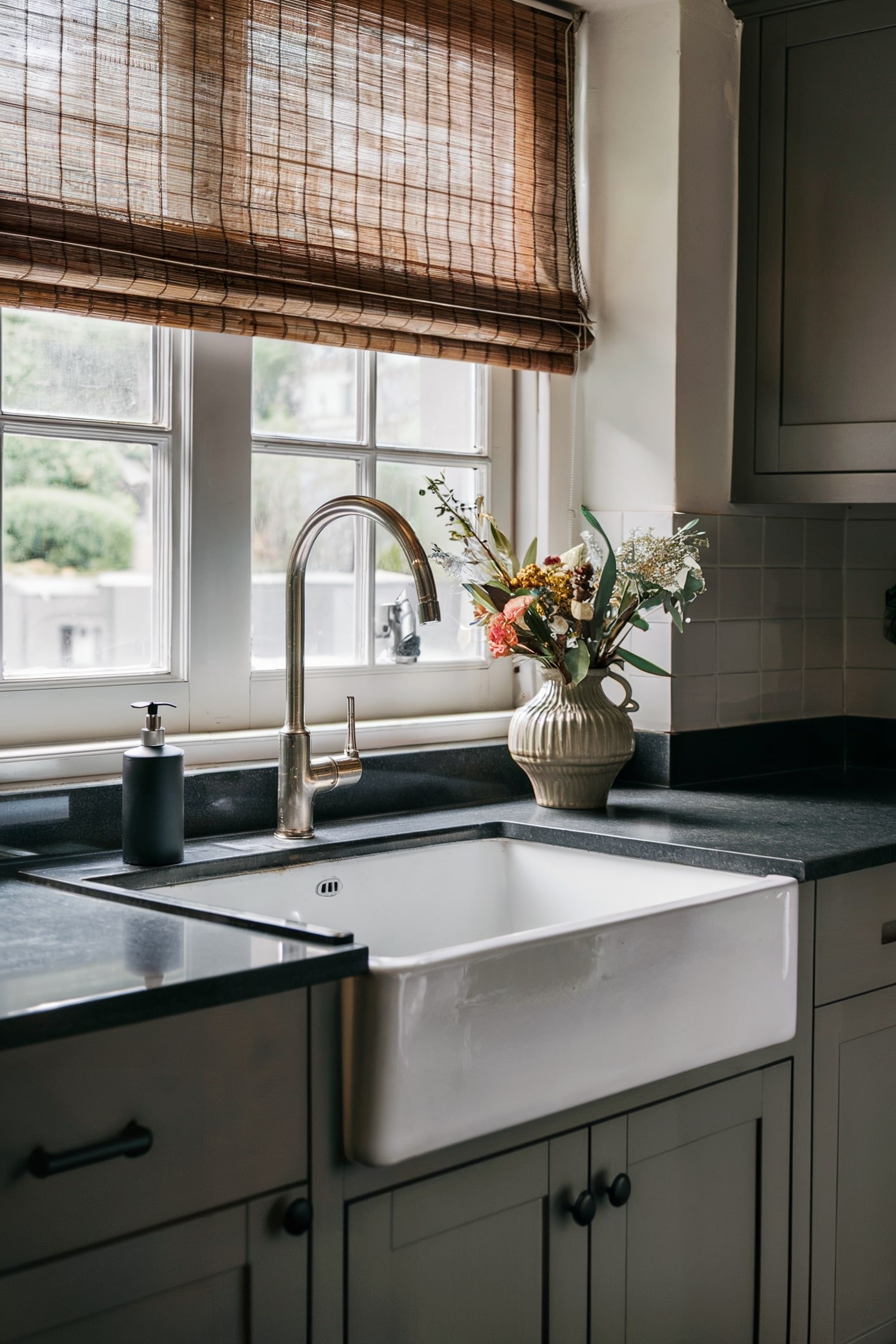 Kitchen sink with bamboo shades and a vase of flowers on the counter