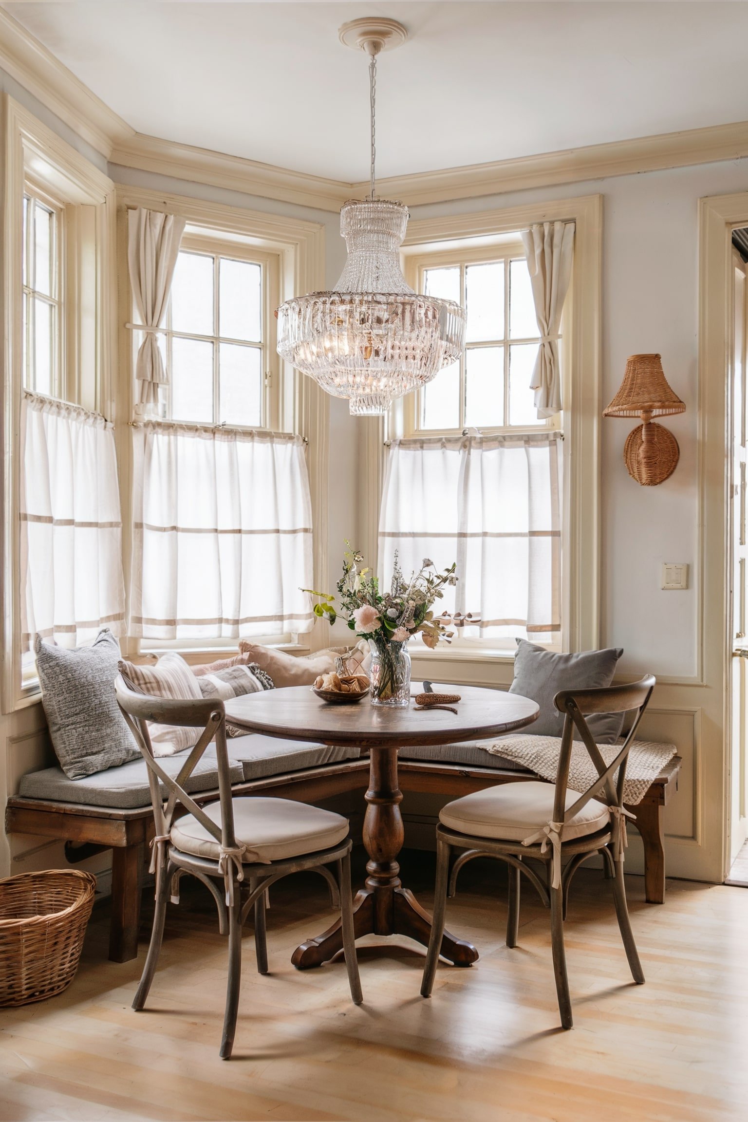 Cozy breakfast nook with white cafe curtains, a crystal chandelier, and a wooden table