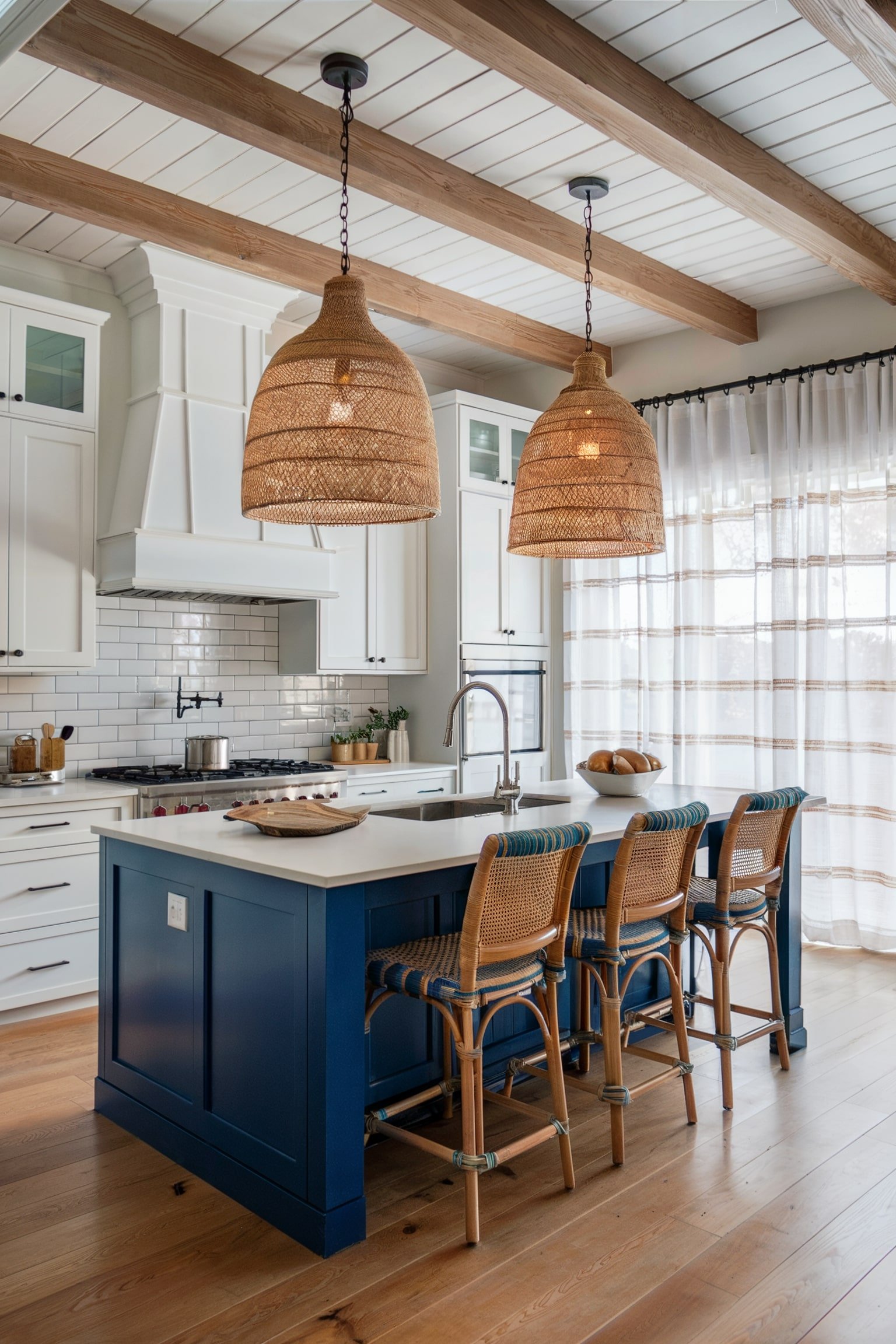 Coastal kitchen with blue island, wicker chairs, and natural light filtering through sheer curtains