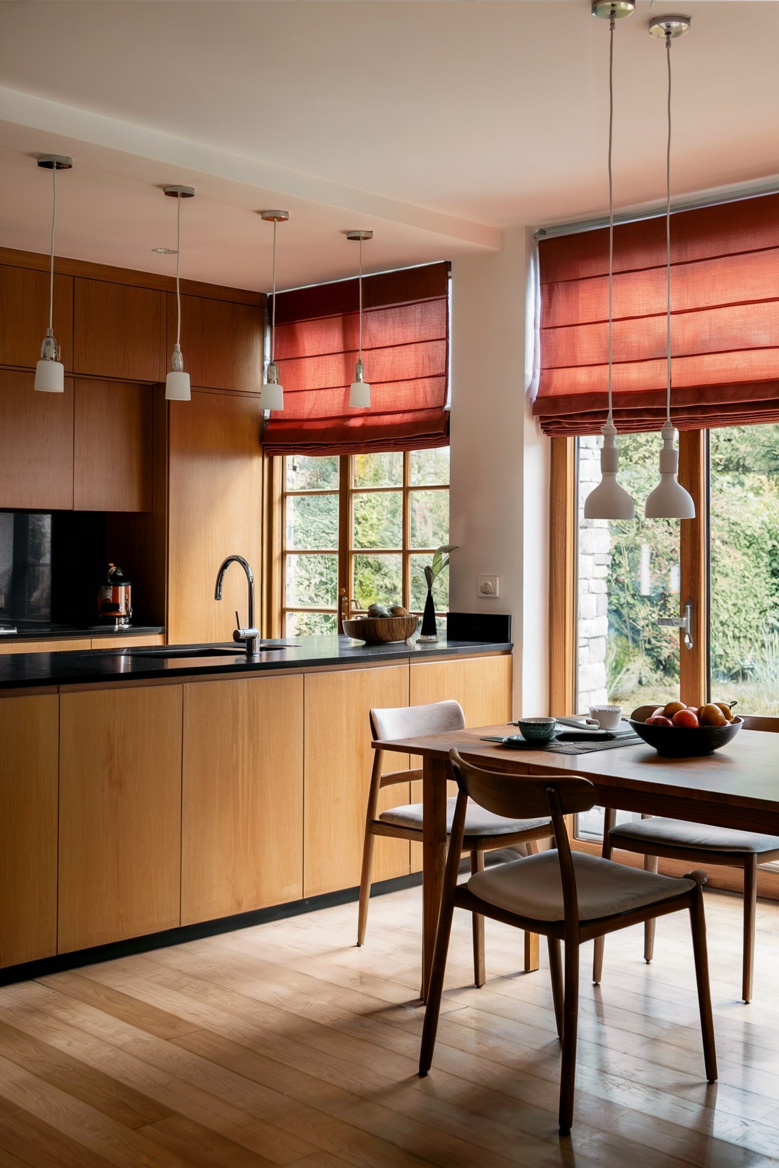 Modern kitchen with wood cabinets, black countertops, and red roman shades