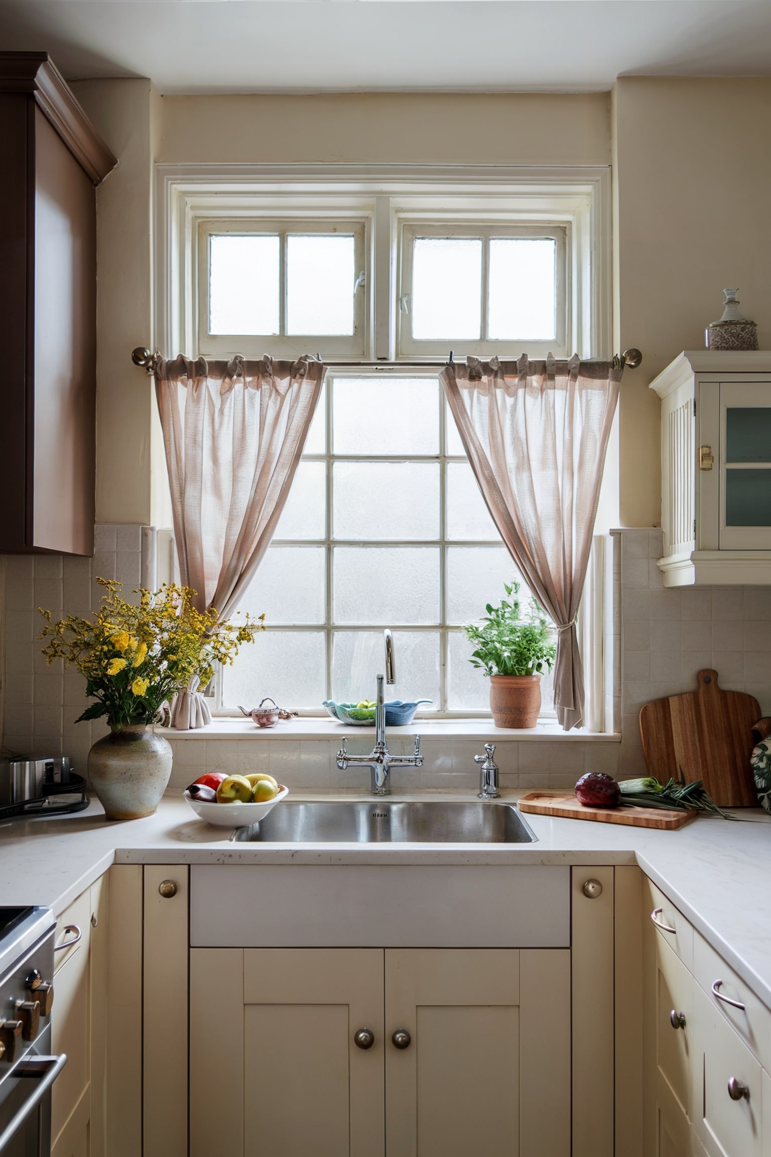 Small window above a sink with beige curtains tied on both sides