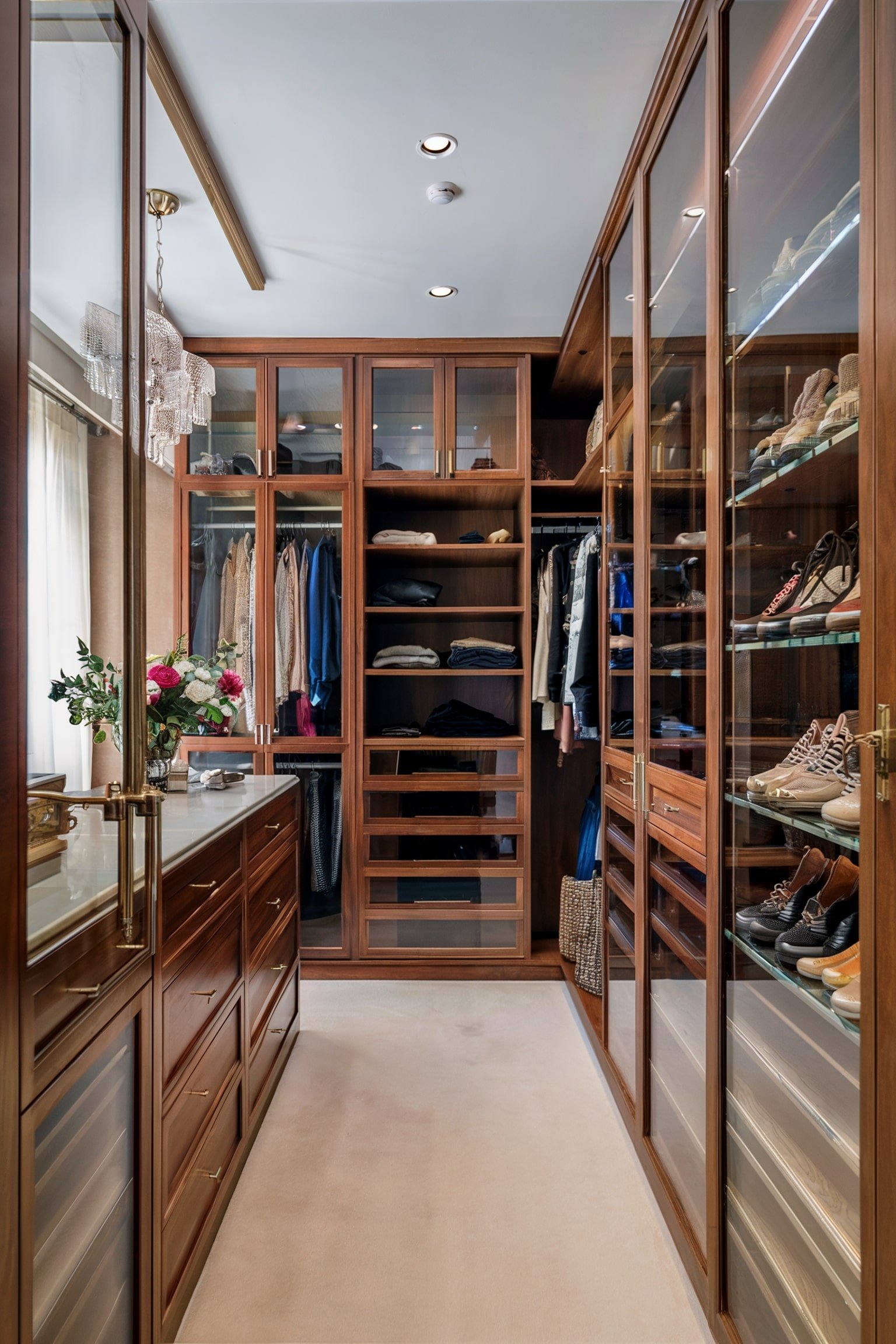 Elegant walk-in closet with glass cabinets, shelves, and a light chandelier above