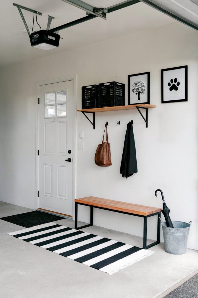 Minimalist garage mudroom with a bench, hooks, shelf, and striped rug