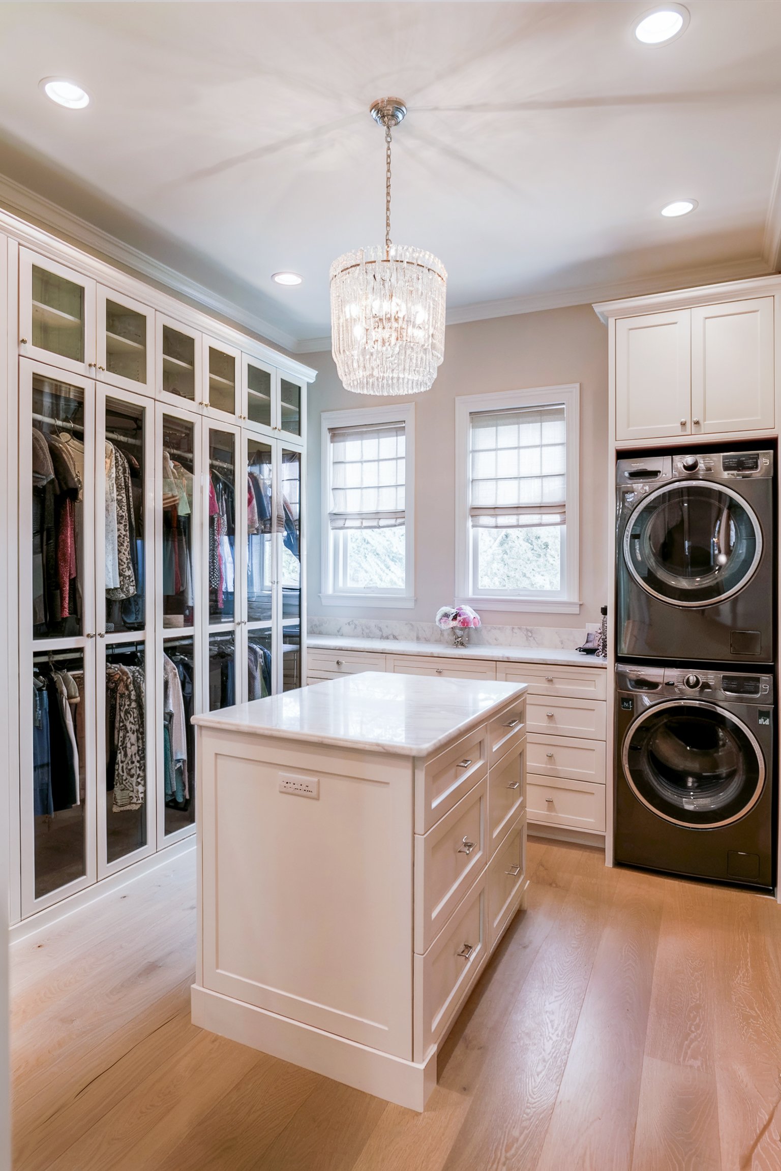 Elegant walk-in closet with a central island, laundry machines, and glass cabinets