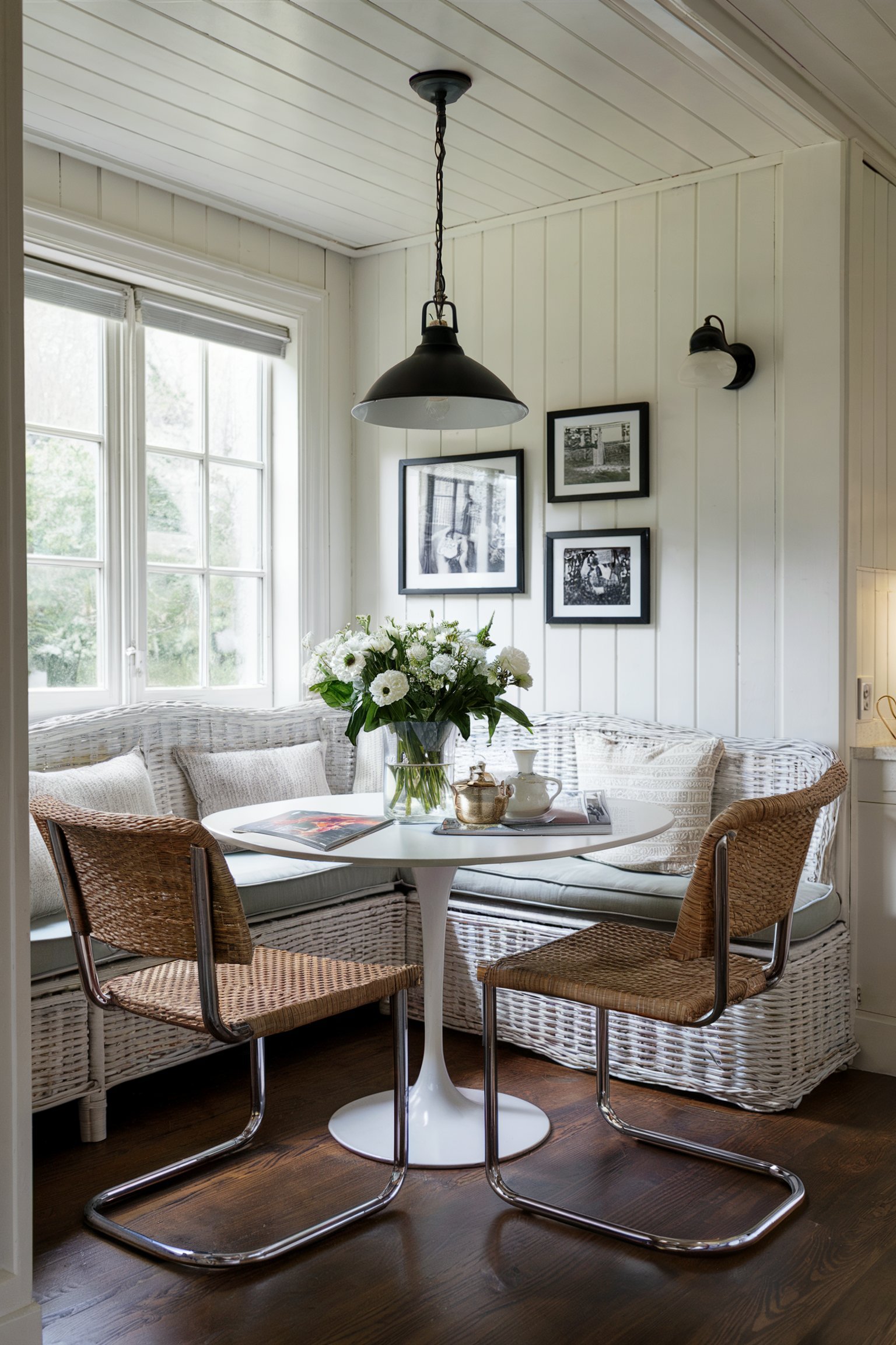 Rustic white wicker banquette seating with a small white round table and black pendant light