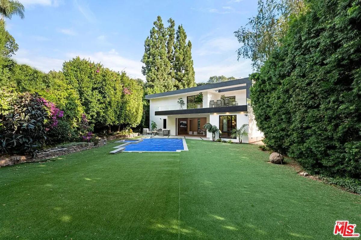 Rear view of the mansion with a pool and a large green lawn.