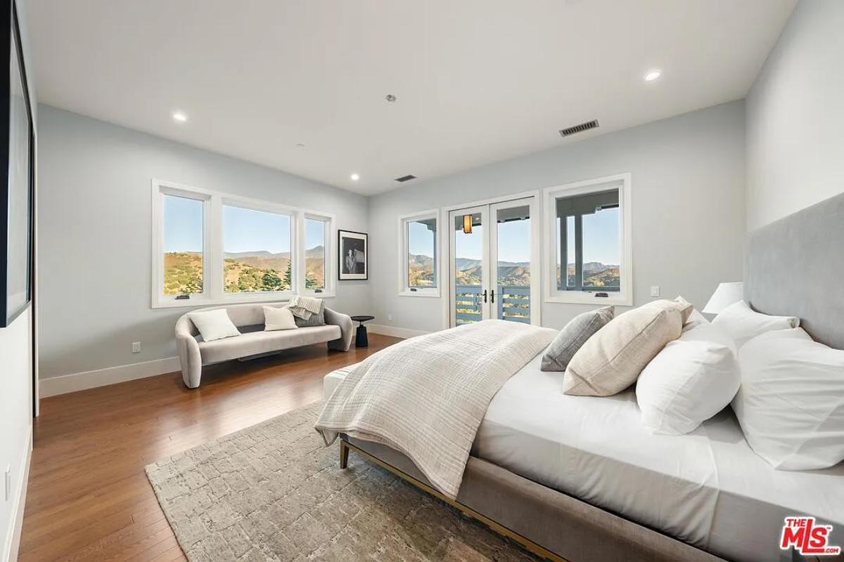 Bedroom with a large bed, glass windows and hardwood floors.