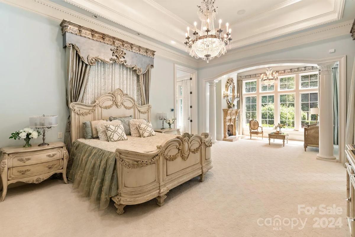 Bedroom with a large bed, chandelier and carpet flooring.