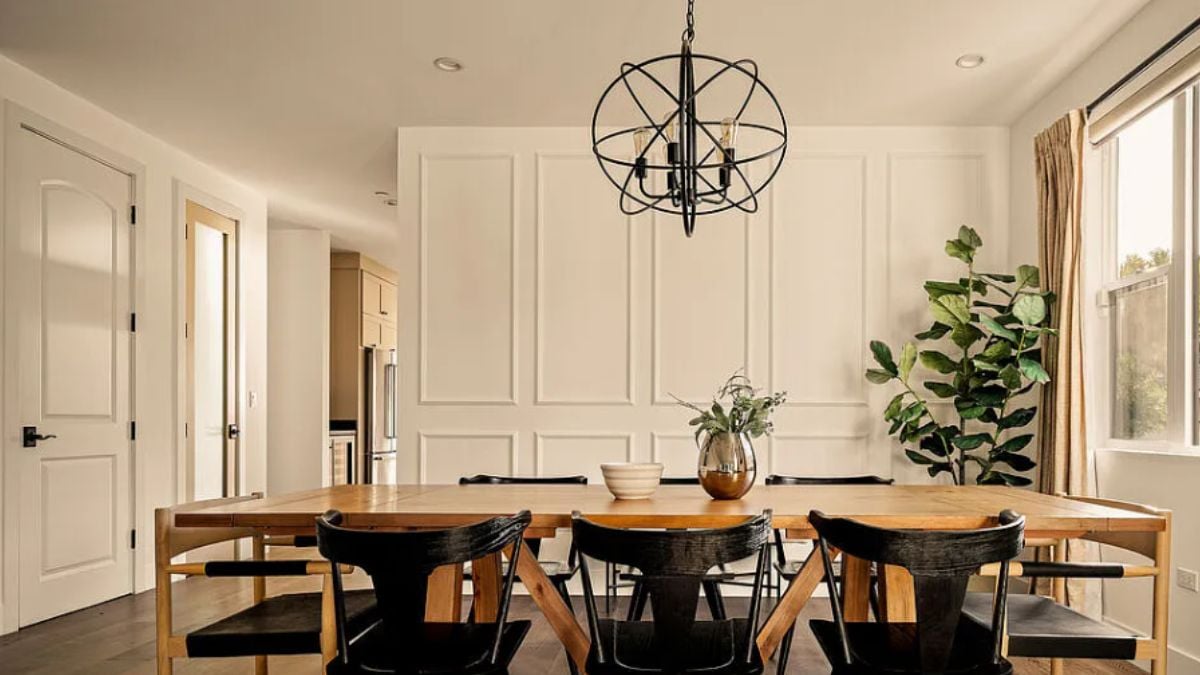 A dining room with windows, a houseplant, a chandelier, and a dining table surrounded by chairs.