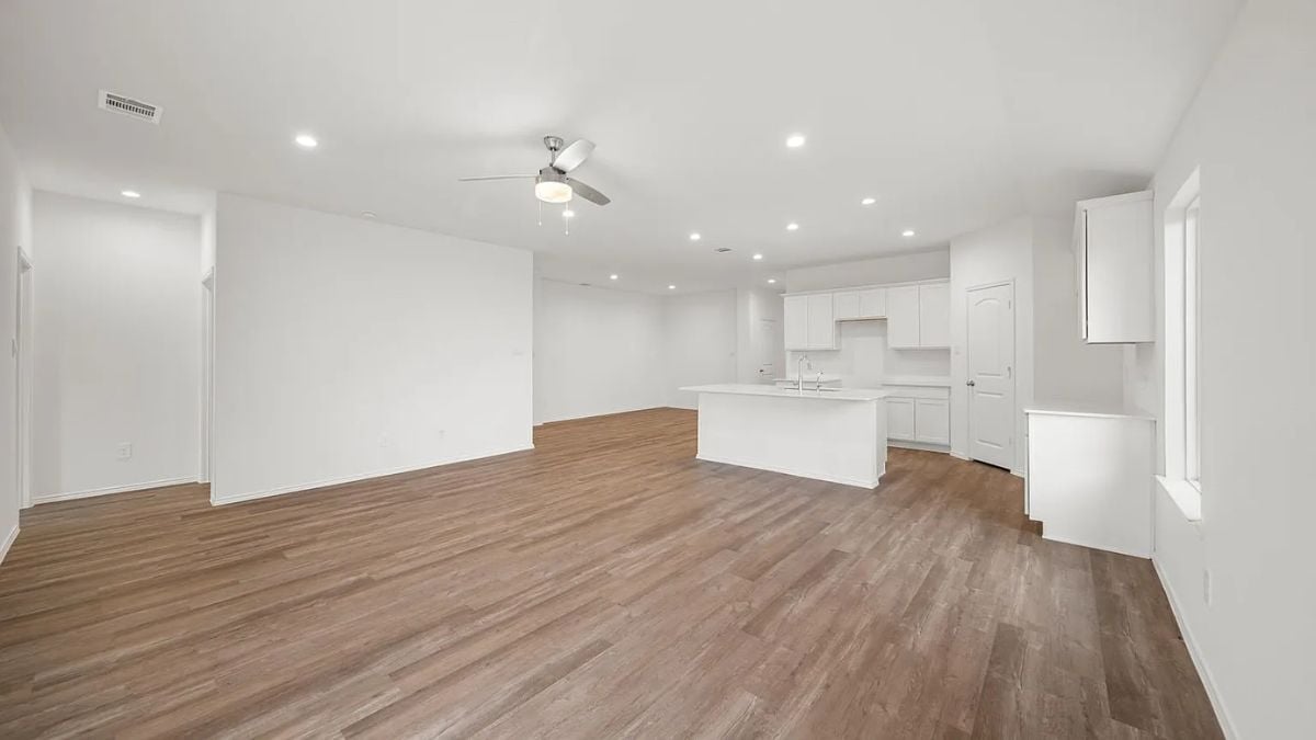 A family room with a wooden floor, white walls, a white ceiling, and an adjacent kitchen.