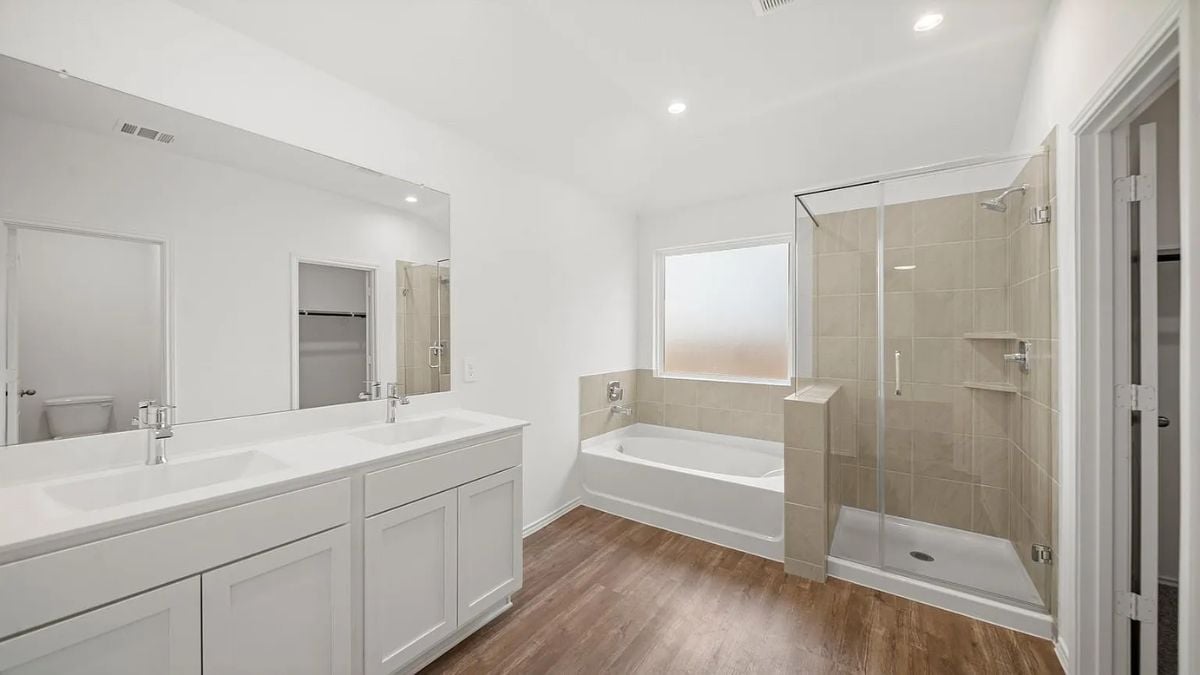 A bathroom with a dual vanity, mirror, cabinets, a bathtub, and a shower room.