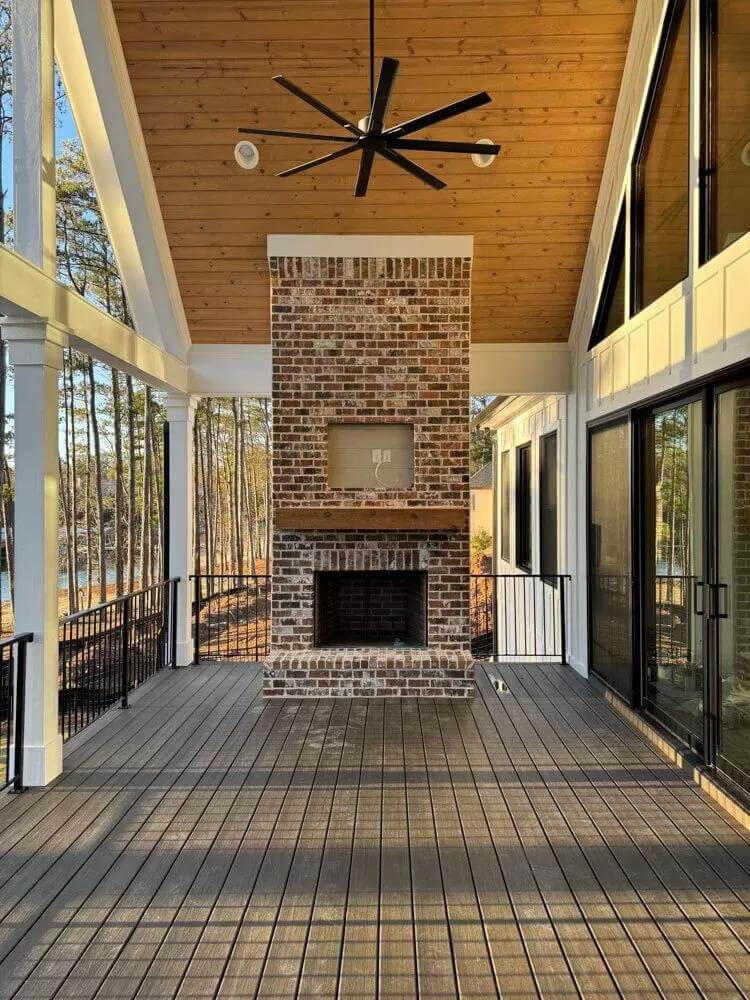 Covered porch with a brick fireplace and an industrial fan that hangs from the wood-paneled ceiling.