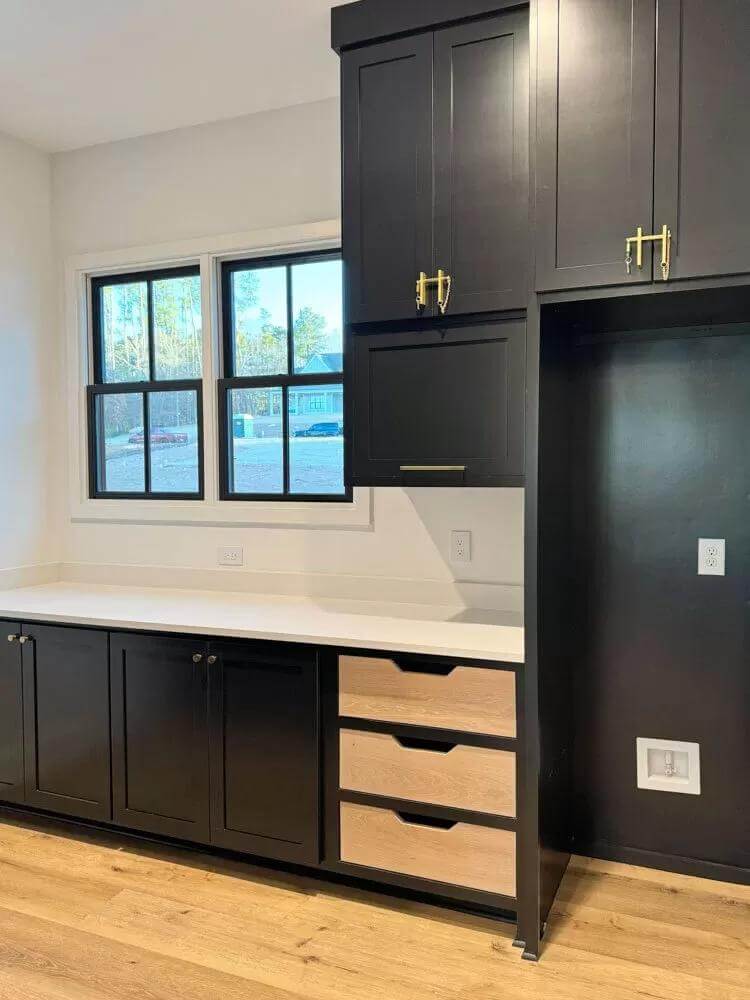Kitchen with black cabinets, wooden drawers, and framed windows.