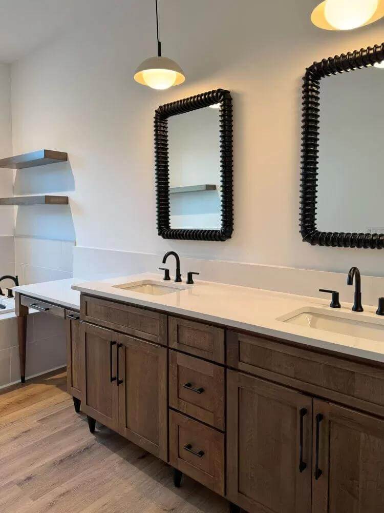 Primary vanity with two sinks, wooden cabinets, and decorative mirrors.