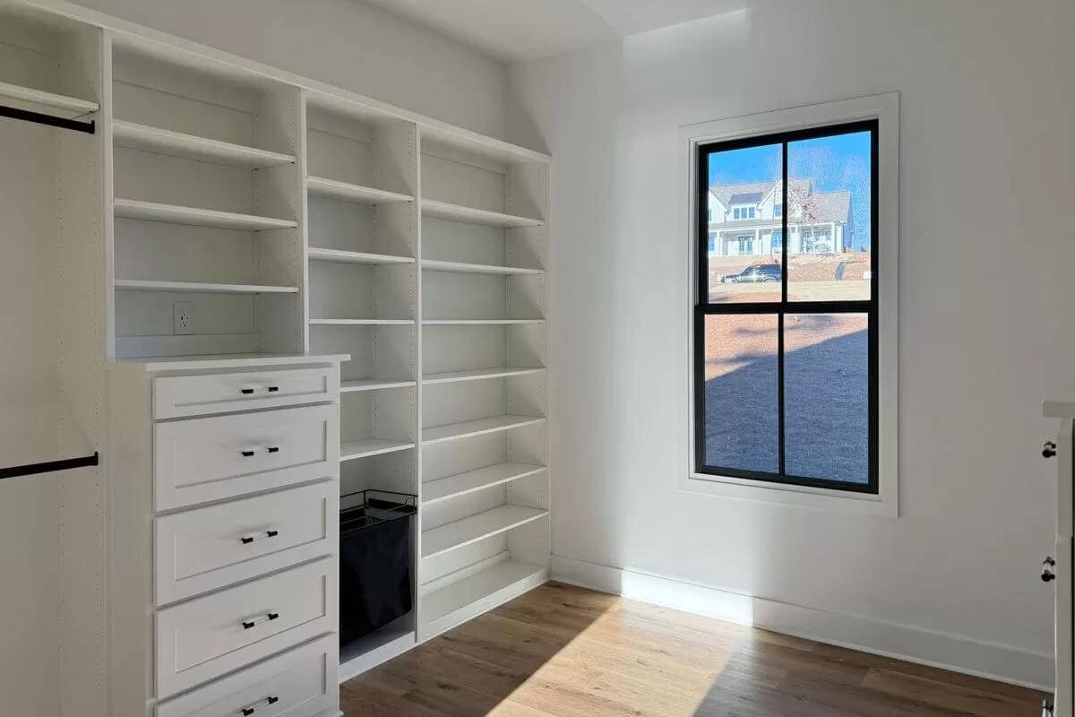 Primary walk-in closet with white built-ins and a black-framed window.