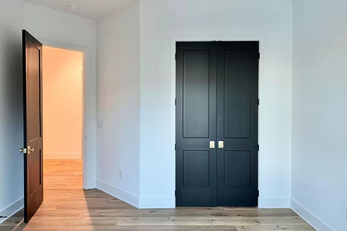 Bedroom with a hardwood floor and a built-in closet with double black doors.