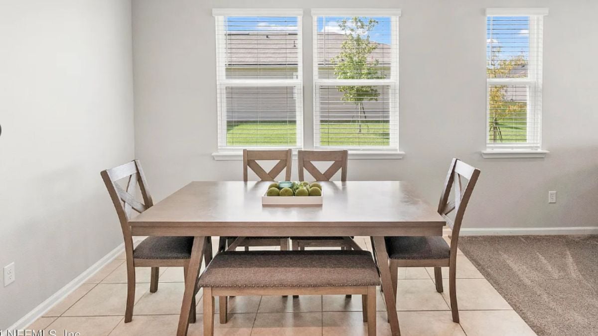A dining room with windows and a dining table surrounded by chairs.