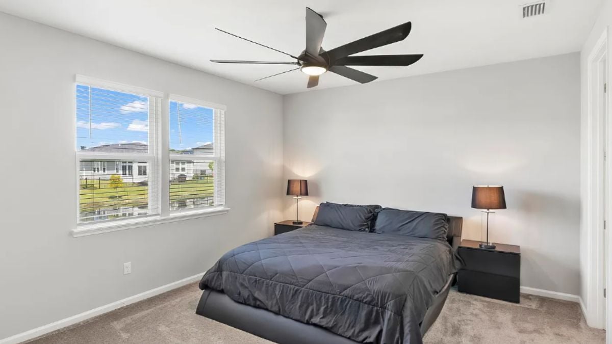 A bedroom with a bed, a window, a ceiling fan, and a nightstand.
