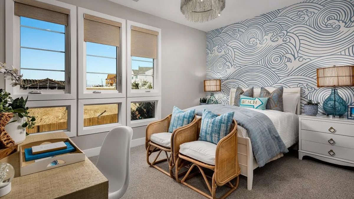 A bedroom with a bed, windows, wallpaper, chairs, and a desk.
