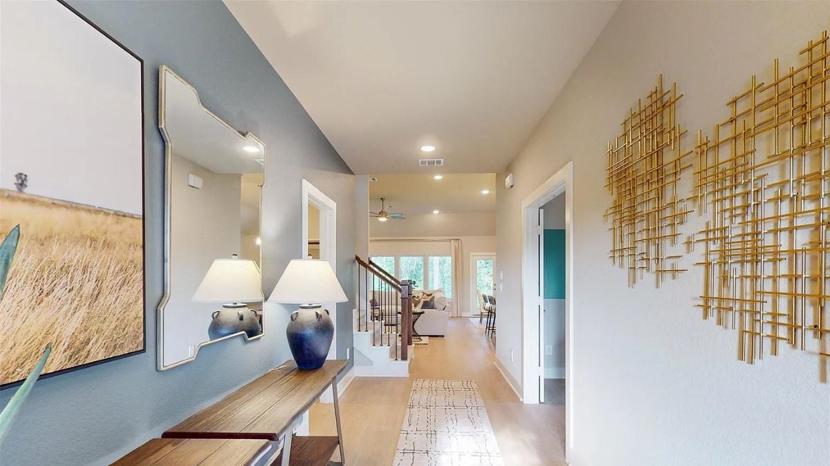 A foyer with a painting, a mirror, a desk, and a lampshade.