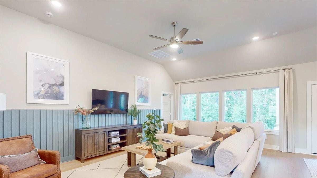 A family room with a ceiling fan, TV, window, paintings, a cabinet, a couch, and a center table.