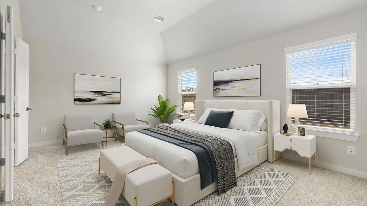 A bedroom with a bed, windows, paintings, a nightstand, a rug, and chairs.