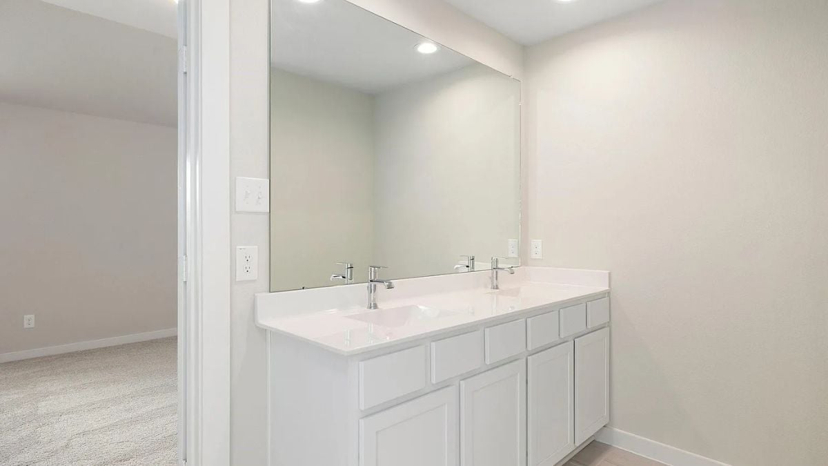 A bathroom with a dual vanity, cabinets, and a mirror.