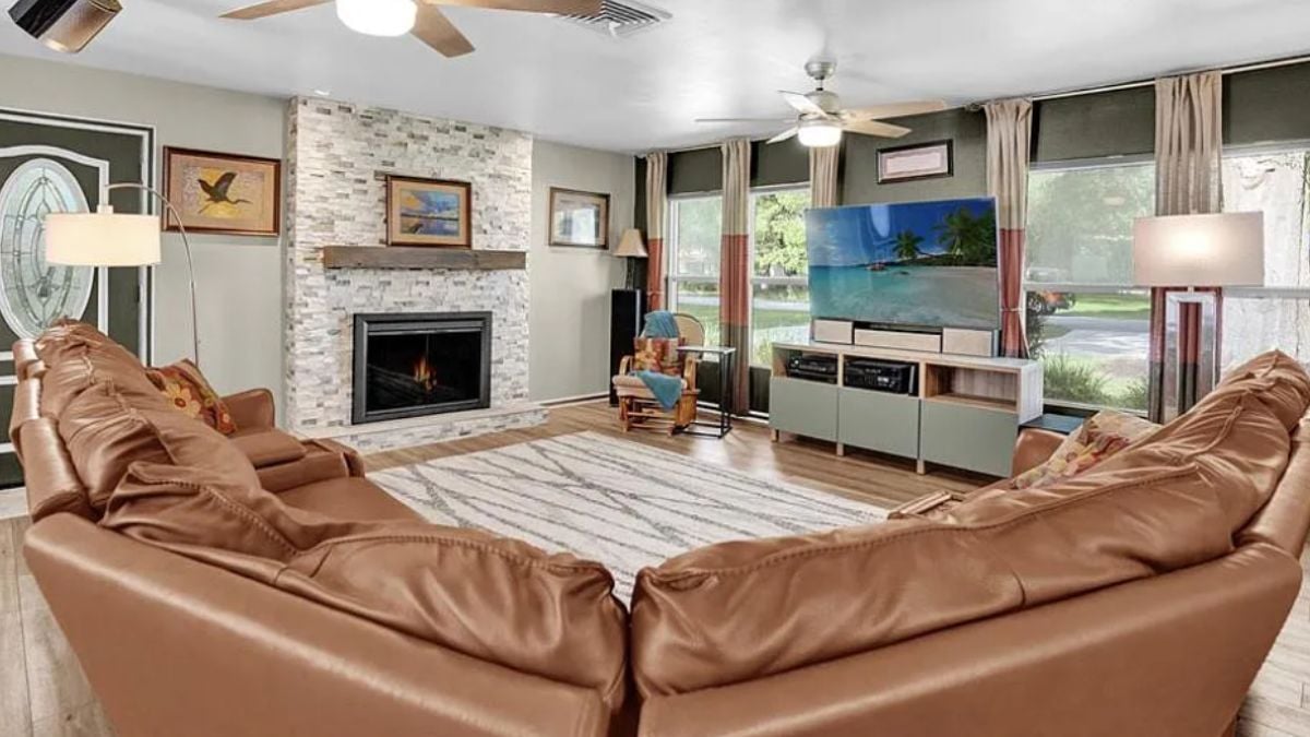 A living room with windows, a fireplace, a TV, a cabinet, a ceiling fan, and a couch.