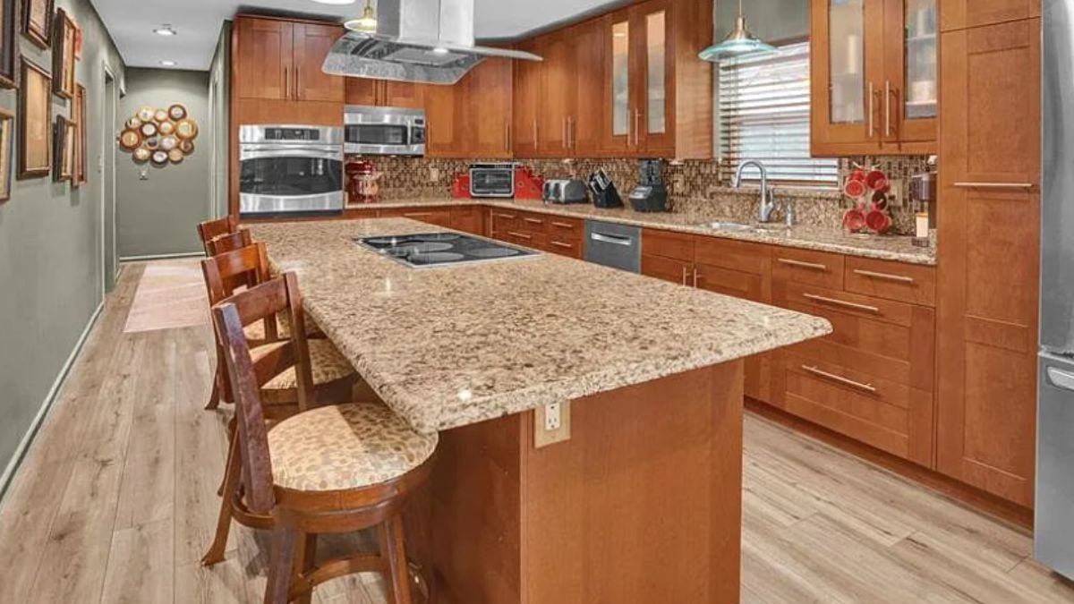 A kitchen with countertops, chairs, a sink, cabinets, and kitchen appliances.
