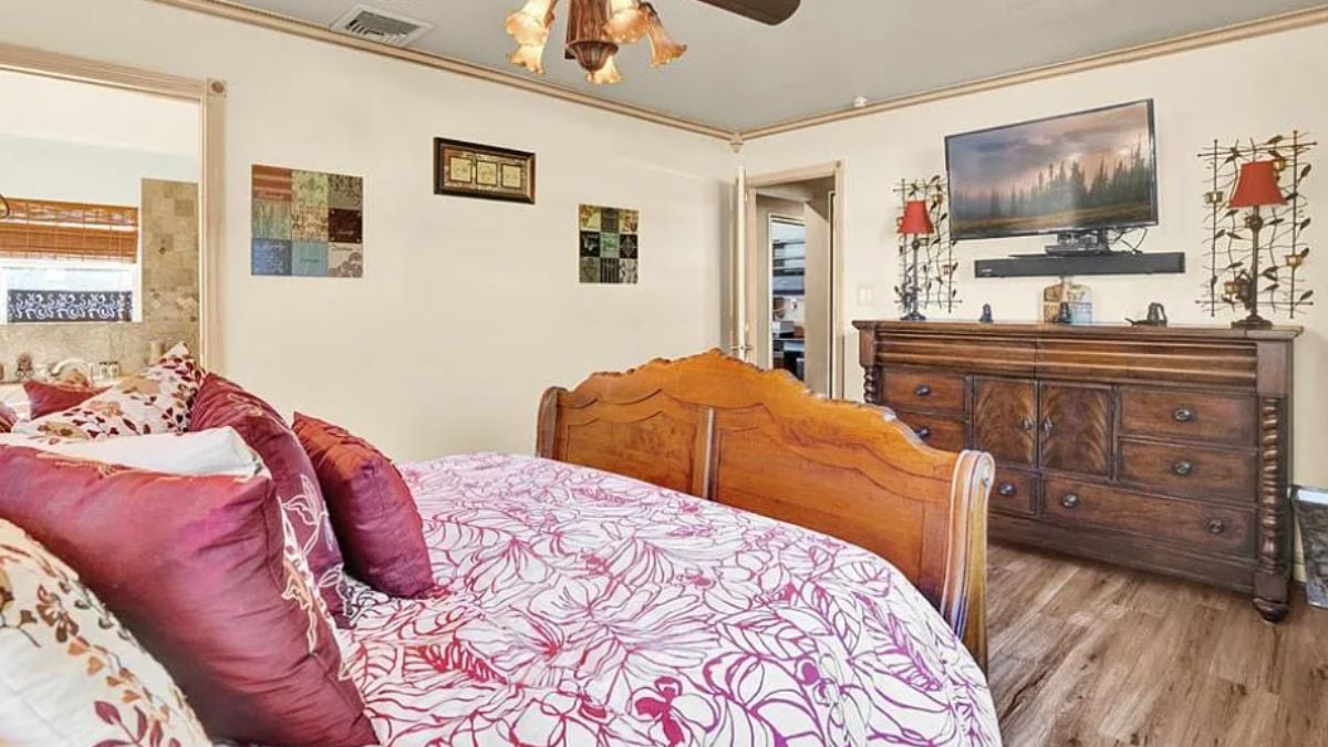 A bedroom with a bed, paintings, a TV, and a cabinet.