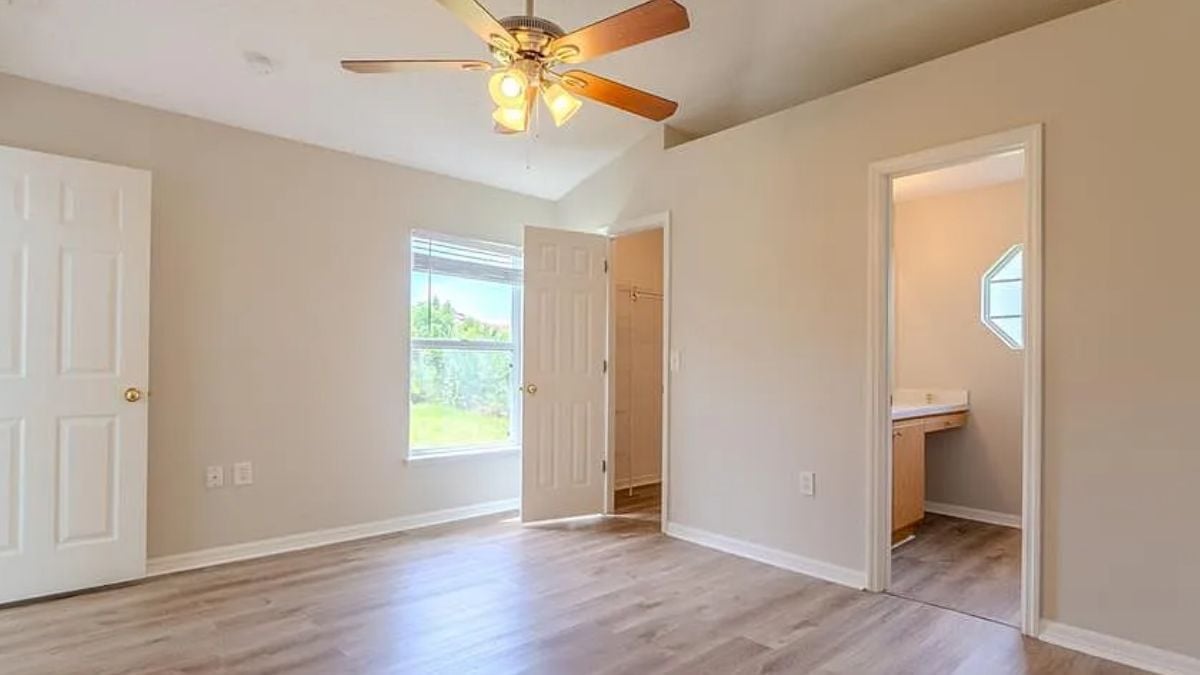 A bedroom with a window, wooden floor and a ceiling fan.