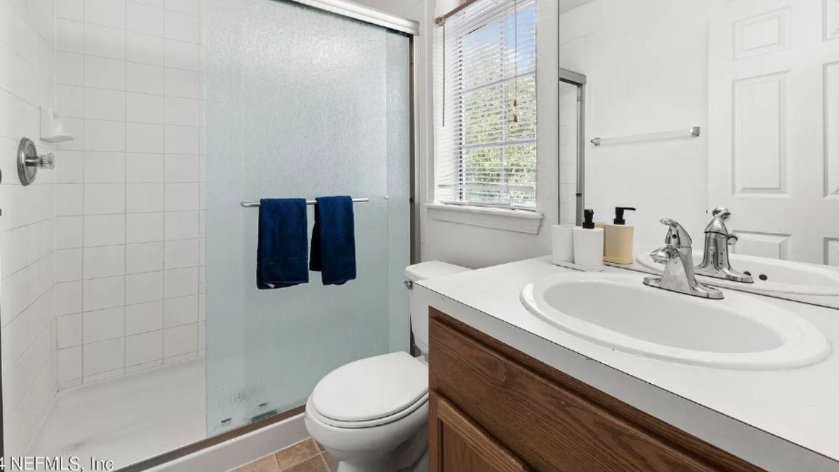 A bathroom with a vanity, shower room, toilet, and mirror.