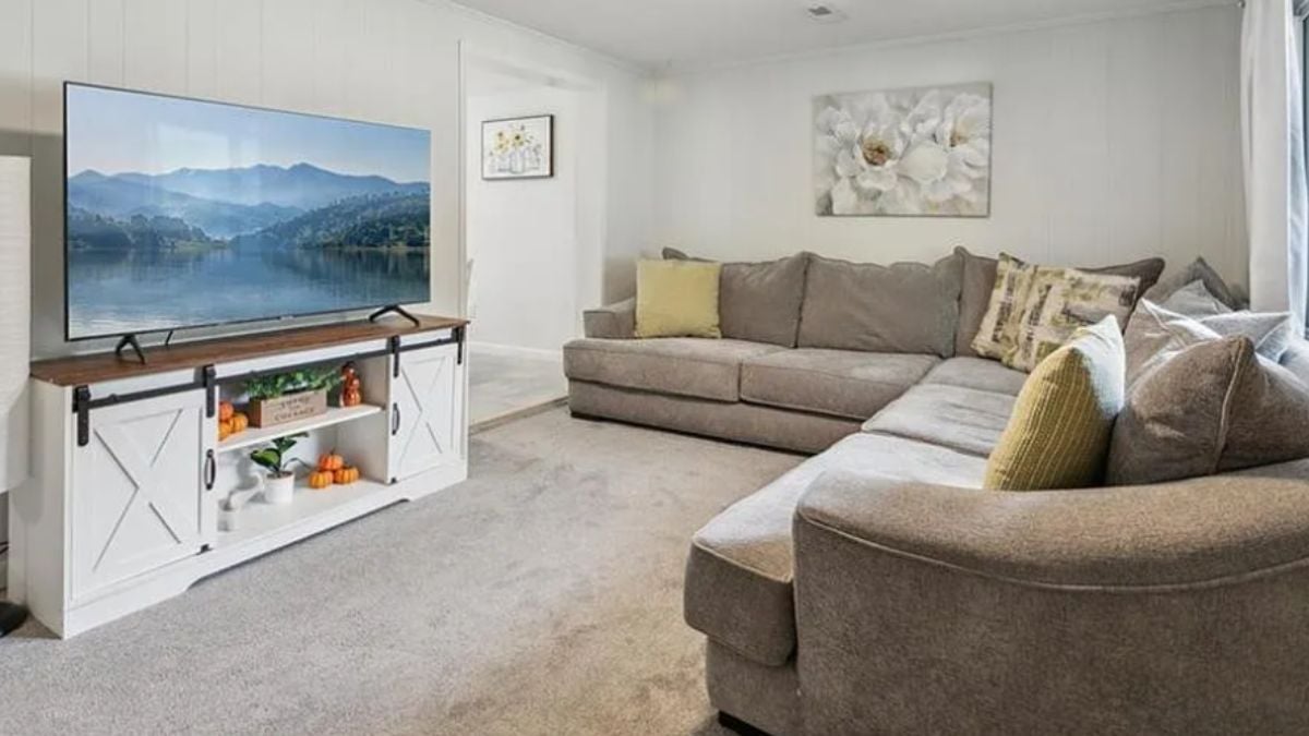 A living room with a TV, a cabinet, a painting, and an L-shaped couch.