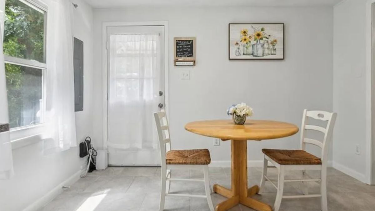 A dining room with a window, a painting, and a round table with chairs.