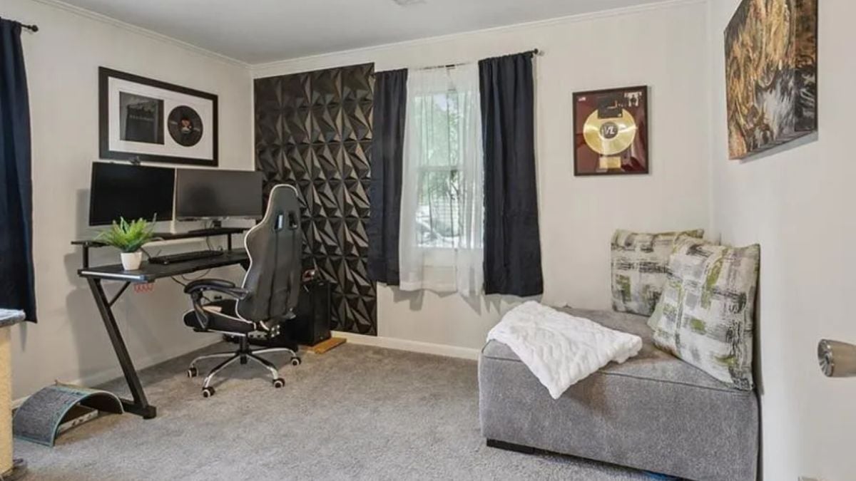 A bedroom with a window, a painting, a couch, a desk, and an office chair.
