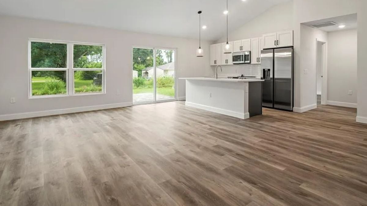 A living room with windows and a kitchen.
