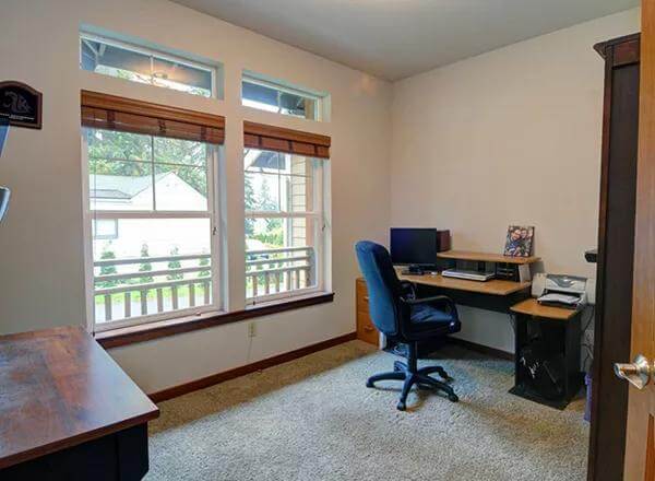 Den with a wooden desk and large windows overlooking the front yard.