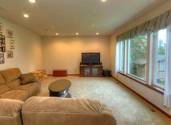 Living room with an L-shaped sofa, a TV, and a carpeted floor.