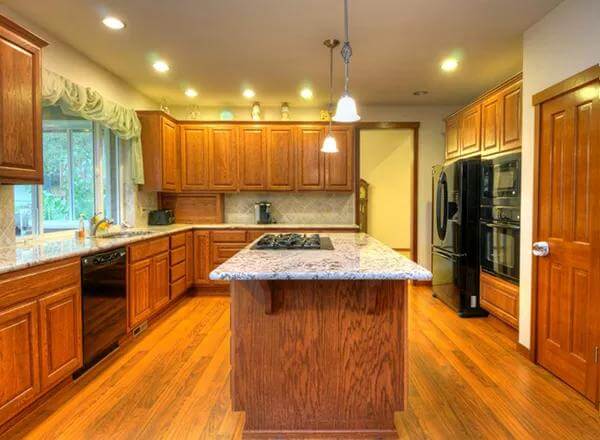 Kitchen with wooden cabinetry and a cooktop island that blends in with the hardwood flooring.