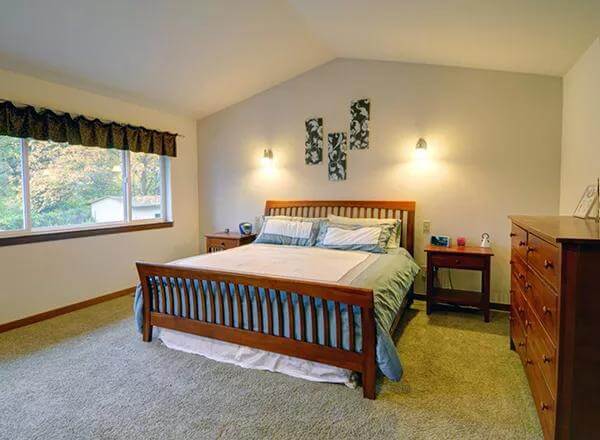 Primary bedroom with a cathedral ceiling and wooden furnishings over the carpeted flooring.