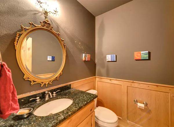 Powder room with wooden wainscoting and a matching vanity adorned by an intricate mirror.