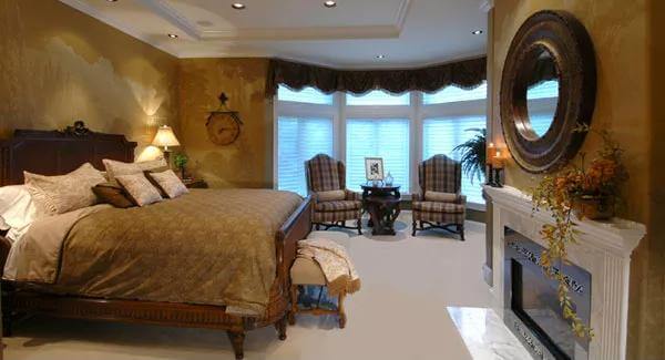 Primary bedroom with a dark wood bed, a fireplace, and a sitting area by the bow window.
