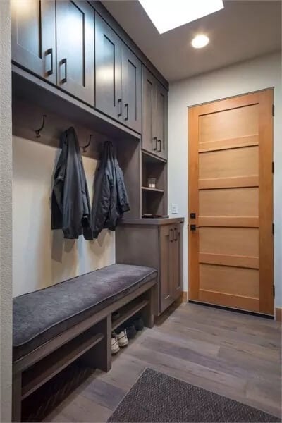 Mudroom with overhead cabinets, coat hooks, and a cushioned bench.