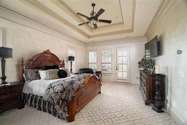 Primary bedroom with wooden furnishings, a wall-mounted TV, and a tray ceiling mounted with an iron fan.