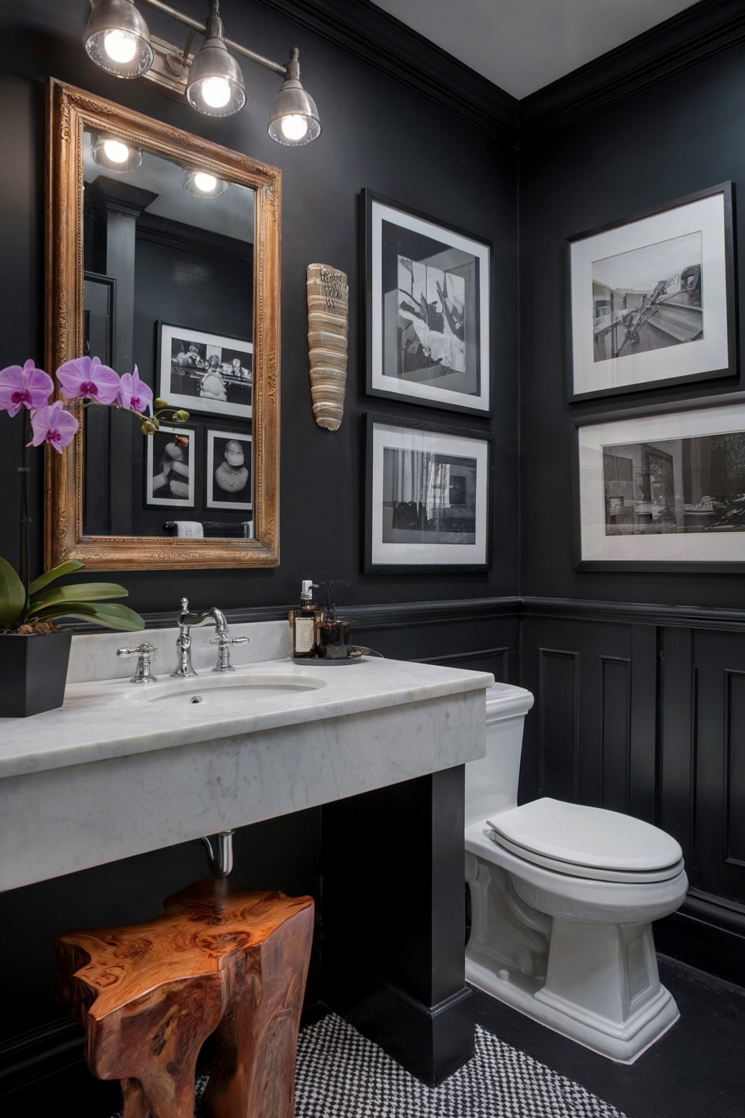 A bathroom with black walls, black-and-white photography, a white marble vanity, and a rustic wood stool